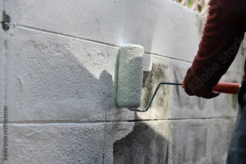 Foto Paint roller applying white coating to concrete wall during exterior renovation