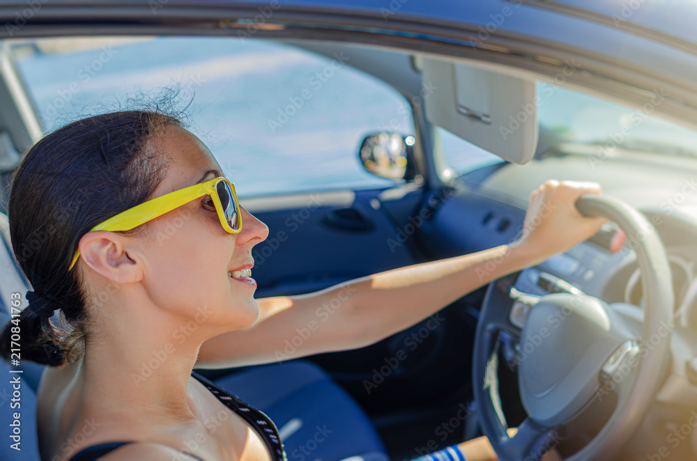 Obraz premium A cheerful woman wearing yellow sunglasses drives a car on a sunny day.