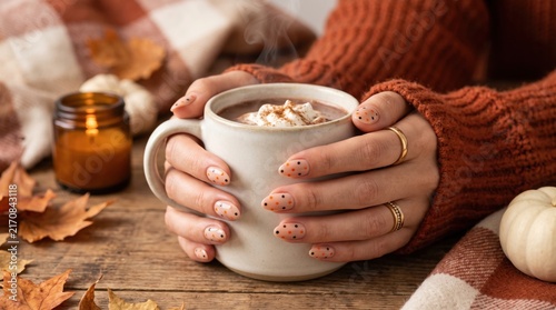 Cozy hands holding a steaming cup of spiced latte with autumn decor and warm tones in the background.