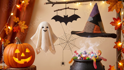 Spooky halloween decorations with a carved pumpkin, a ghost, a witchs hat, a cauldron full of candy, and a bat hanging from a branch, creating a festive atmosphere