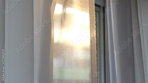Soft golden evening sunlight glowing through a translucent white curtain moving gently in the breeze, creating a dreamy abstract interior background.
