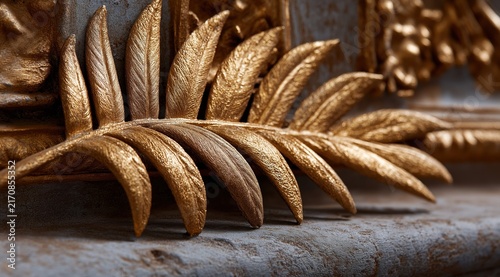 Close up of a golden leaf carving on a weathered stone surface. Classical architectural ornament with metallic gold palm frond relief