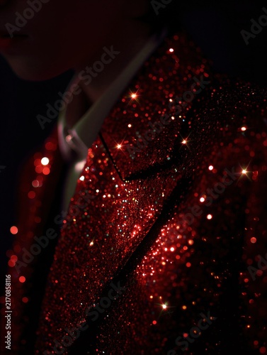 Close up of a red glittery sequin jacket. Vertical photo of a person in sparkling reflective fabric with star shaped light flares. Fashion and party celebration concept