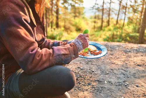 woman eating breakfast at a campsite with golden forest light behind