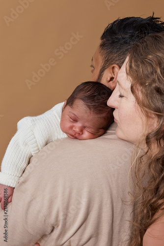 Intimate Portrait Of Interracial Family With Newborn Baby Resting On Father's Shoulder