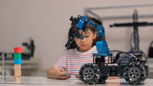 Asian girl student programming robotic arm car with digital tablet in STEM classroom. Science technology engineering mathematics education, creative robotics coding and smart school concept.