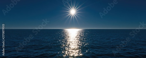 Brilliant sun shines, reflecting a dazzling path across the calm ocean surface