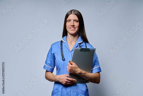 Canvastavla Smiling female nurse holding clipboard with patient records standing against gre