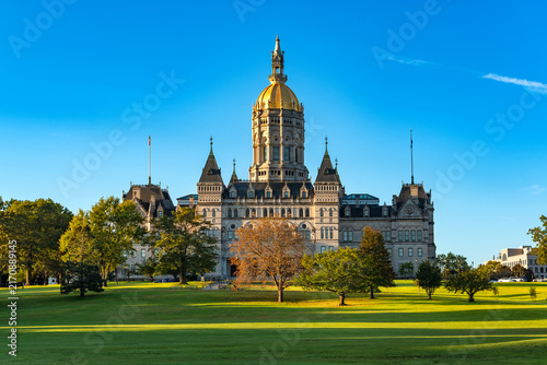 The historic Connecticut State Capitol building with its bright gold dome sits on the expansive green lawn of Bushnell Park in Hartford, Connecticut.