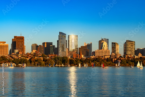 Sunlight reflects off modern glass skyscrapers of Back Bay and the Beacon Hill area in Boston as sailboats glide along the calm waters of the Charles River.