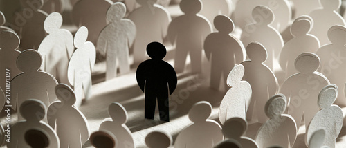 A lone black paper cutout figure stands out prominently amidst a vast crowd of white paper cutouts, powerfully symbolizing individuality, uniqueness, diversity, and the concept of standing