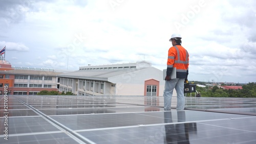 Asian male technician in hardhat checking rooftop photovoltaic solar panel and inverter control box with toolbox. Clean renewable energy generation, sustainable eco power system and ESG concept.