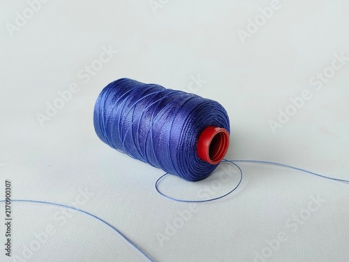Plakat blue sewing thread spool on white background with loose thread