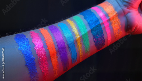Colorful makeup swatches on skin against dark background
