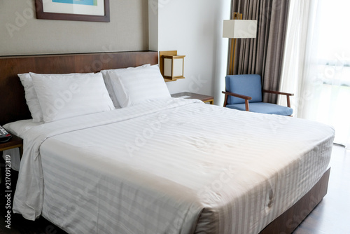 Modern hotel bedroom interior with comfortable bed and blue armchair