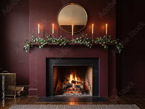 fireplace interior with burning fire, candles and eucalyptus garland on burgundy wall