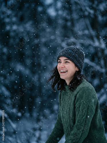 Smiling woman in a green knit sweater in a snowy forest in winter in soft daylight