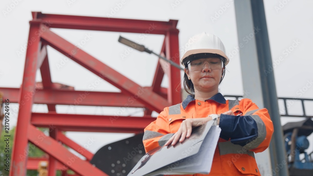 Fototapeta premium Asian female technician in hardhat checking factory wastewater treatment facility and drainage basin with clipboard. Industrial water management, ESG environmental sustainability concept.