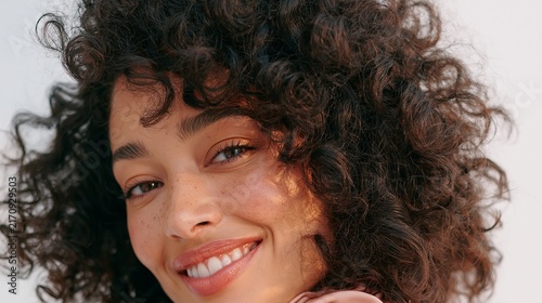 Close up portrait of a smiling woman with voluminous curly dark hair against a plain white background.