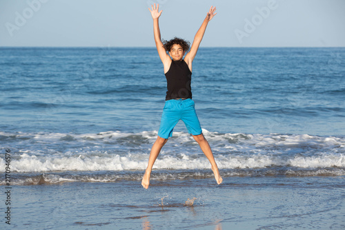 Принти на полотні Happy teenager jumping mid-air on a sunny ocean beach with arms raised in joy