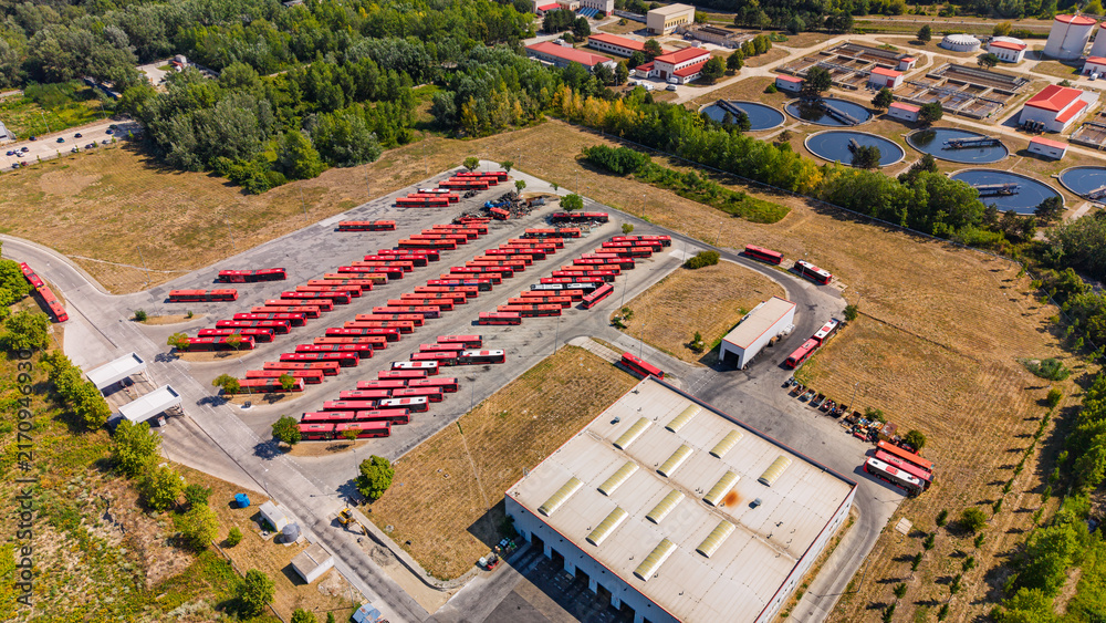 Obraz premium Public transport bus depot. Numerous red buses park in organized rows on an asphalt parking lot next to a maintenance building.