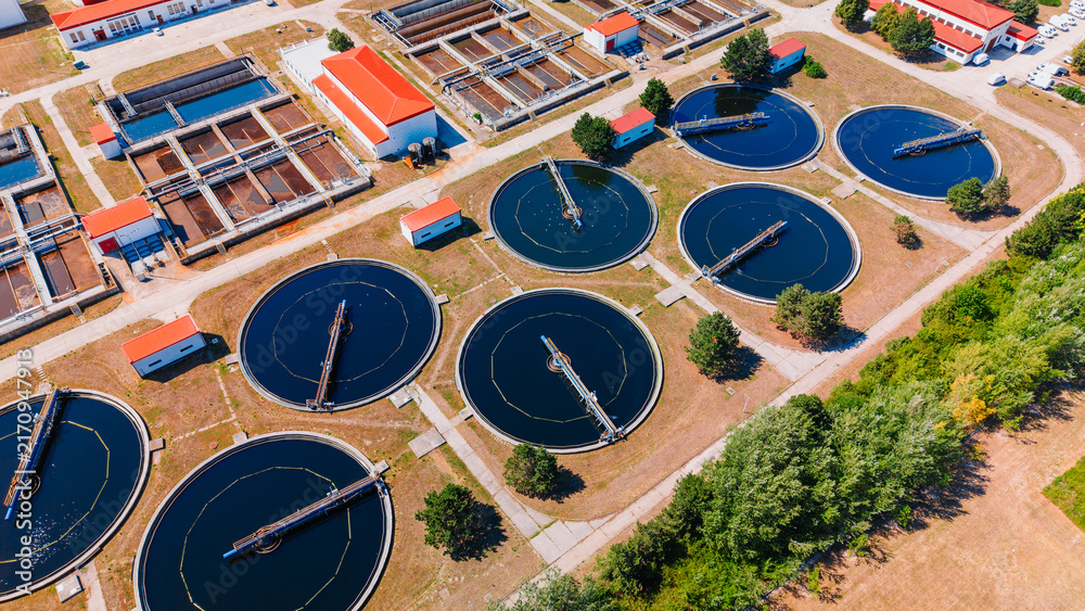 Naklejka premium Water treatment facility shown from above with round tanks and buildings. The image shows a water treatment facility with large round tanks and several buildings. The tanks are arranged neatly.