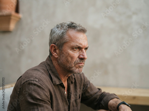 Middle aged man in a linen shirt seated at an outdoor stone courtyard table