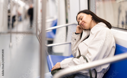 Young woman is sitting and dozing in in half-empty tram wagon, getting to work. Girl travels in urban transport, whiles away time on trip.