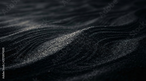 Dark black sand beach background featuring rippled sand texture and dune patterns.