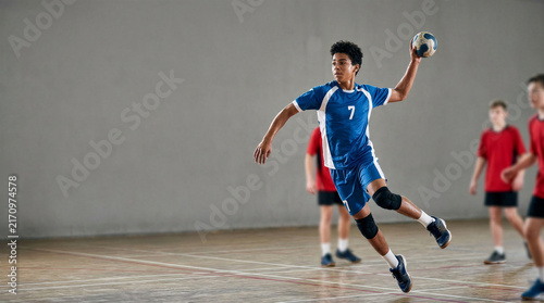 Young boy playing handball and jumping in a sports hall  