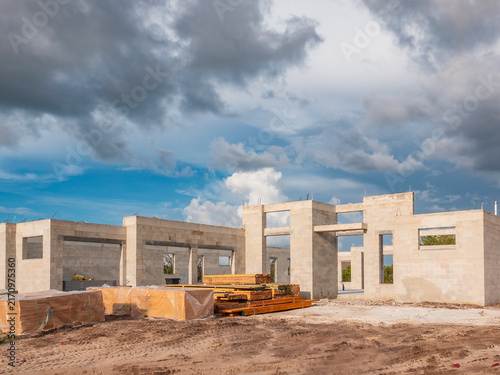 Construction site of a single-family house in progress, with stacks of lumber and shrink-wrapped panels stacked near front entrance, in a suburban residential development in southwest Florida