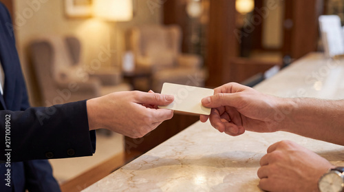 Friendly receptionist handing hotel key card to guest at counter desk with helpful service and welcoming professional mood