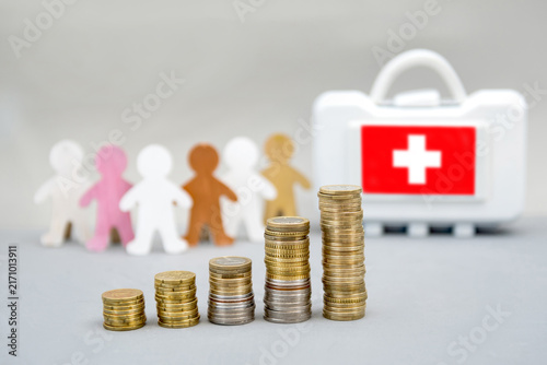 Obraz na płótnie Growing stacks of coins in front of diversity people, a first aid kit