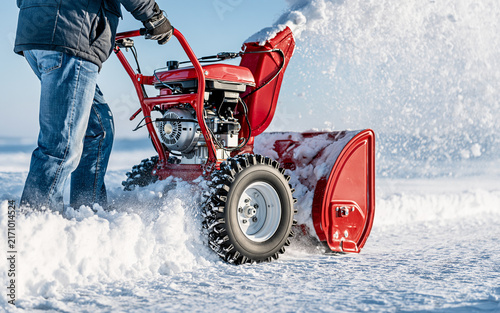 Person operating red snow blower to clear snow from driveway in winter