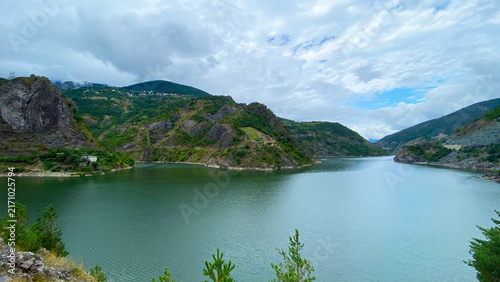 Coruh River opens through mountain valley, wide landscape view of green water, rocky slopes and rural homes in Turkey