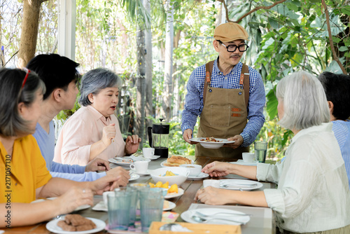 Konstfotografi Senior group receives food from waiter at garden cafe reunion, sharing lunch and conversation around table while attentive service, friendship, relaxed social connection shape mealtime, aging society