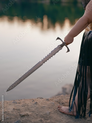 Obraz na płótnie Woman Hand Holding Fantasy Sword near Lake Close-Up Outdoor