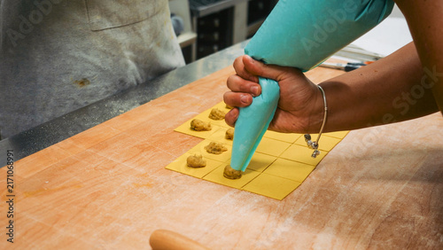 фотографія Chef hand using a piping bag, filling fresh pasta squares with traditional torte