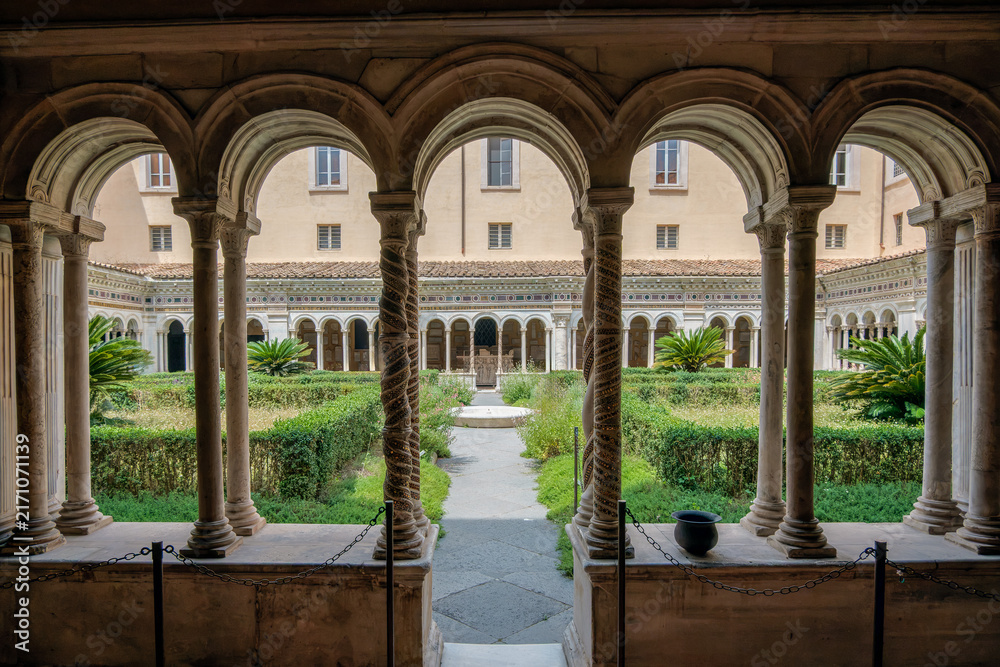 Fototapeta premium View through medieval cloister arcade and cosmatesque spiral columns into the inner garden at the Basilica of Saint Paul Outside the Walls in Rome Italy