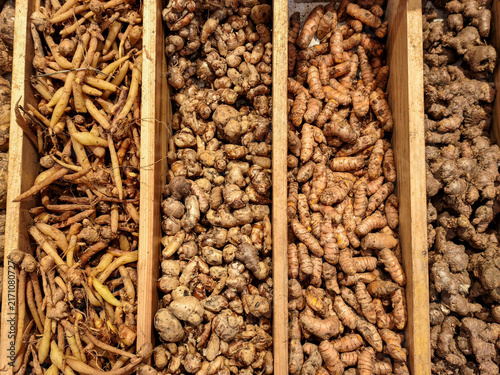 Raw Fresh Asian Rhizomes and Spices Display. An overhead view of wooden bins filled with organic raw ginger, turmeric, galangal, and fingerroot roots at a traditional market.