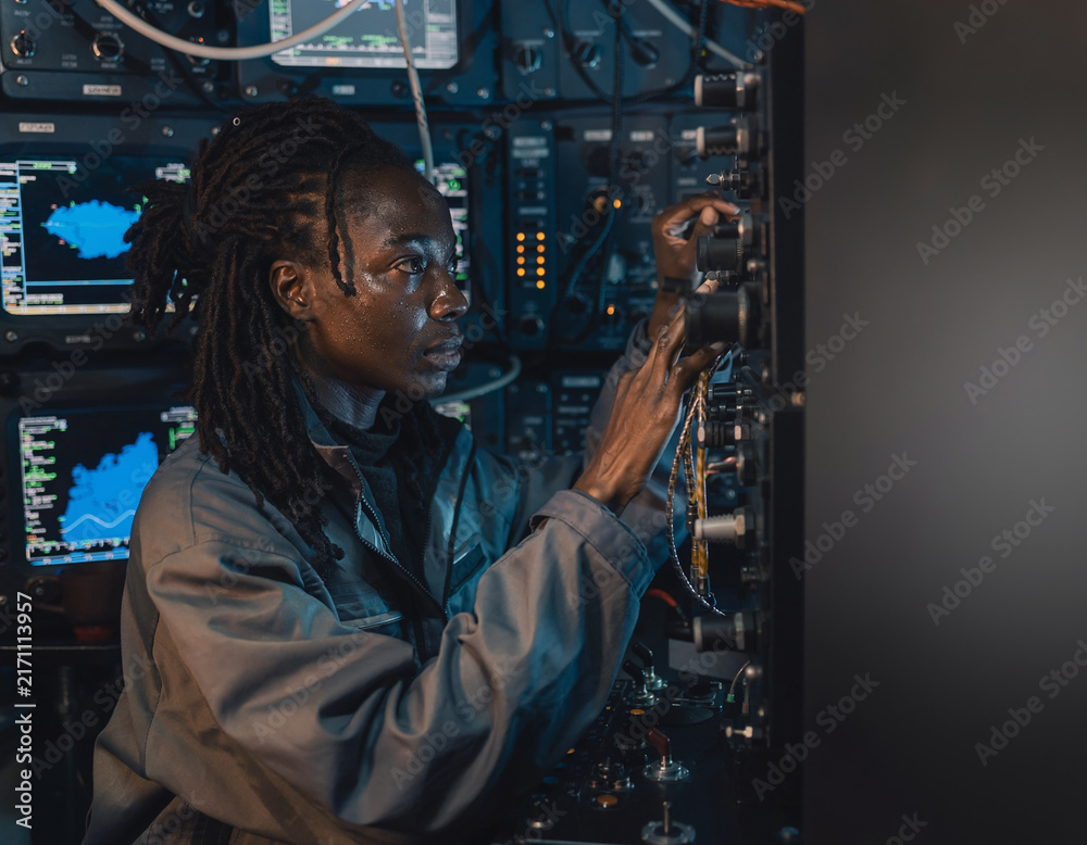 Fototapeta premium Female black engineer adjusting complex wiring and control panels in dark technical server room
