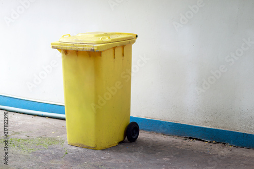 Konstfotografi Large yellow wheeled garbage bin with lid placed outdoors beside a building, was