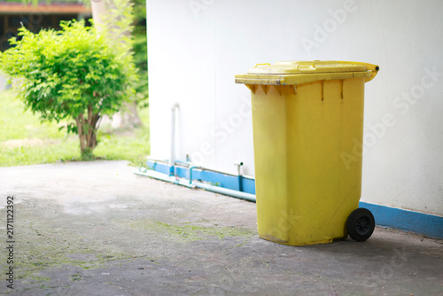 Canvastavla Large yellow wheeled garbage bin with lid placed outdoors beside a building, was