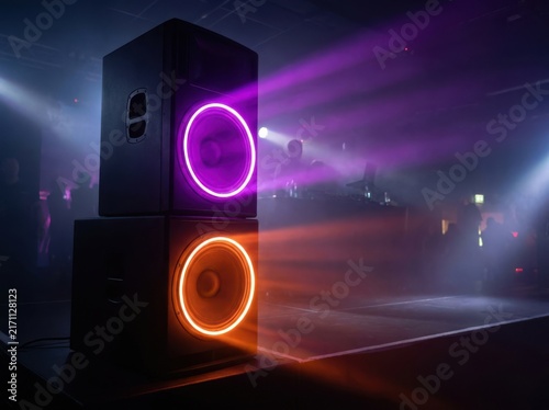 Large professional audio speakers glowing with vibrant neon lights in dark club