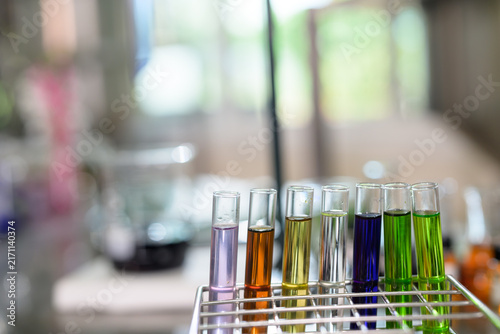 Test tubes filled with various colored liquids are neatly arranged in a metal rack in a laboratory setting.