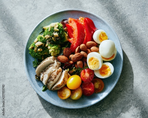 A healthy balanced meal plate featuring grilled chicken breast sliced avocado boiled eggs kidney beans and fresh colorful cherry tomatoes