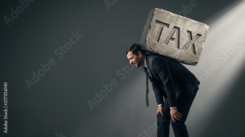 Man carrying heavy tax burden stone on back, financial stress concept
