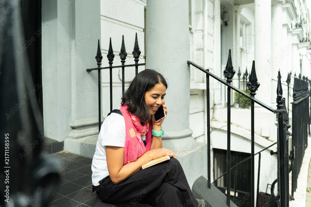 Fototapeta premium Woman making phone call sitting on steps in London, enjoying conversation and urban connectivity