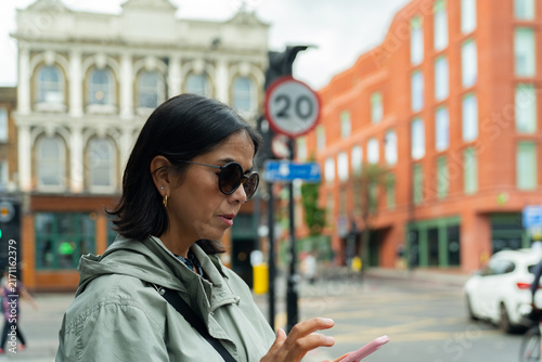 Photography Asian woman using smartphone for navigation in urban London street, looking for