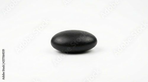 Dark oval pebble or stone on white background with black stone smooth rock dark mineral river pebble zen stone spa rock polished pebble stone object natural mineral material meditation